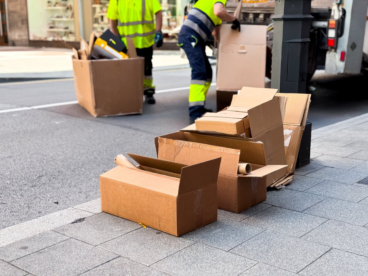 Workers dispose of cardboard boxes on a city street sidewalk