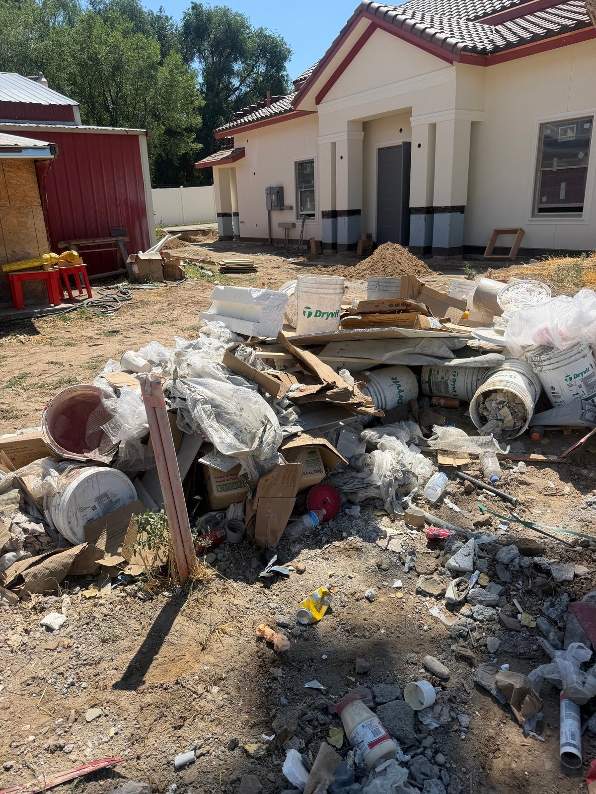 Construction debris and waste materials on the ground in front of a house under renovation
